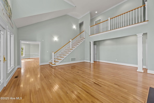 unfurnished living room with light hardwood / wood-style floors, ornate columns, ornamental molding, and a towering ceiling