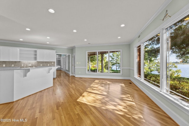 kitchen featuring light hardwood / wood-style flooring, tasteful backsplash, a breakfast bar area, white cabinets, and ornamental molding