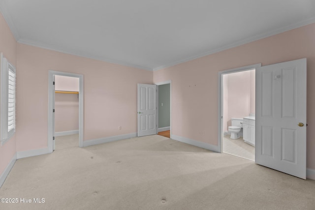 unfurnished bedroom with a closet, a spacious closet, crown molding, ensuite bathroom, and light colored carpet