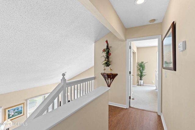 hallway with a textured ceiling, baseboards, and wood finished floors