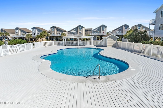 community pool with a residential view, fence, an outdoor structure, and a shed