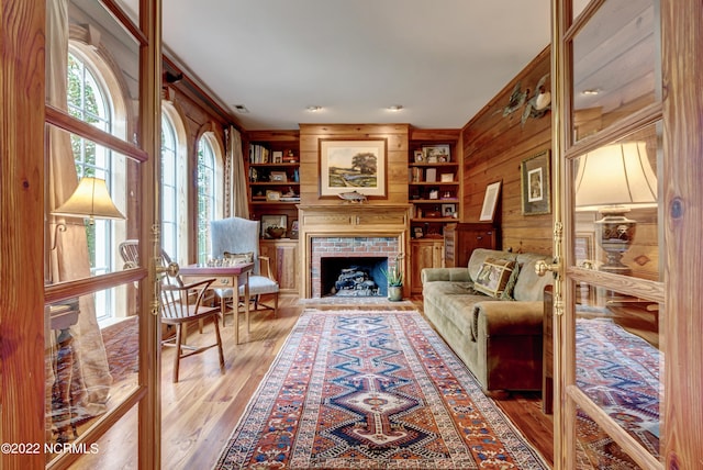 living room featuring wooden walls, built in shelves, a fireplace, plenty of natural light, and hardwood / wood-style floors