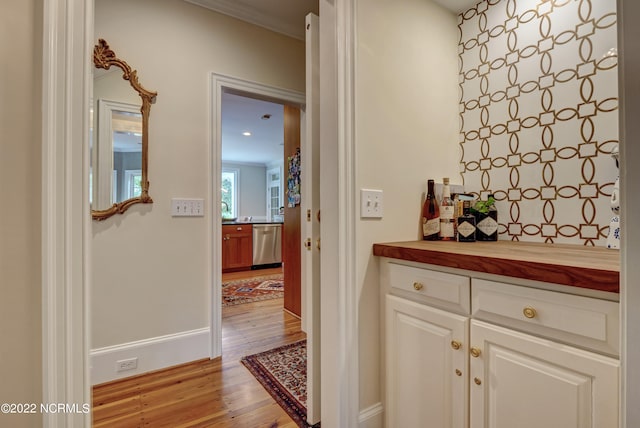 bar with light hardwood / wood-style flooring, stainless steel dishwasher, crown molding, and white cabinets