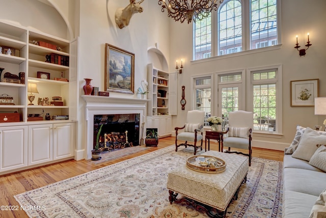 living room featuring built in features, an inviting chandelier, a high ceiling, and light hardwood / wood-style floors