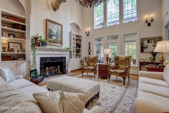 living room featuring an inviting chandelier, light hardwood / wood-style floors, a towering ceiling, a fireplace, and built in shelves