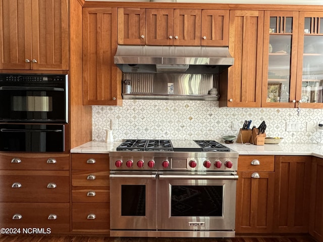 kitchen with backsplash, light stone counters, wall chimney exhaust hood, range with two ovens, and black double oven