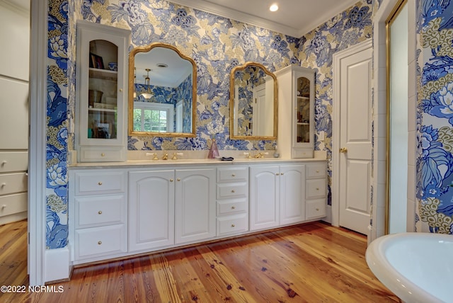 bathroom featuring ornamental molding, hardwood / wood-style flooring, vanity with extensive cabinet space, and double sink