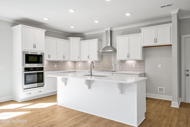 kitchen featuring built in microwave, stainless steel oven, wall chimney range hood, and a center island with sink