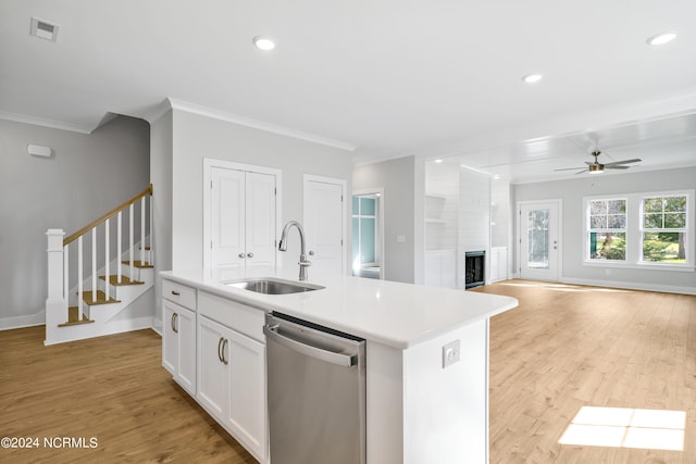 kitchen with sink, white cabinetry, stainless steel dishwasher, a large fireplace, and a kitchen island with sink