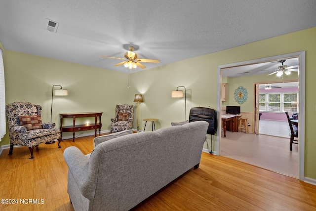 living room with ceiling fan, a textured ceiling, and light hardwood / wood-style flooring