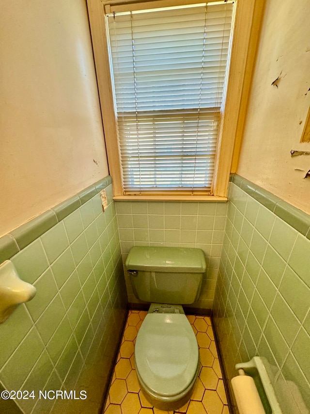 bathroom with tile flooring, toilet, and tile walls