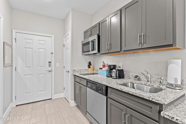 kitchen featuring stainless steel appliances, light tile floors, sink, light stone countertops, and gray cabinets