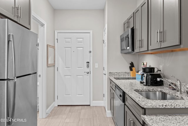 kitchen featuring appliances with stainless steel finishes, light tile flooring, sink, light stone countertops, and gray cabinets