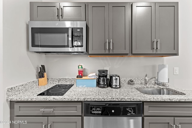 kitchen with sink, stainless steel appliances, light stone counters, and gray cabinetry