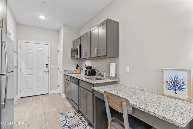 kitchen with appliances with stainless steel finishes, sink, a kitchen breakfast bar, gray cabinets, and light stone counters