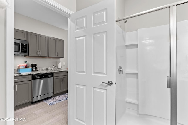 kitchen with appliances with stainless steel finishes, light stone counters, light hardwood / wood-style floors, sink, and gray cabinets