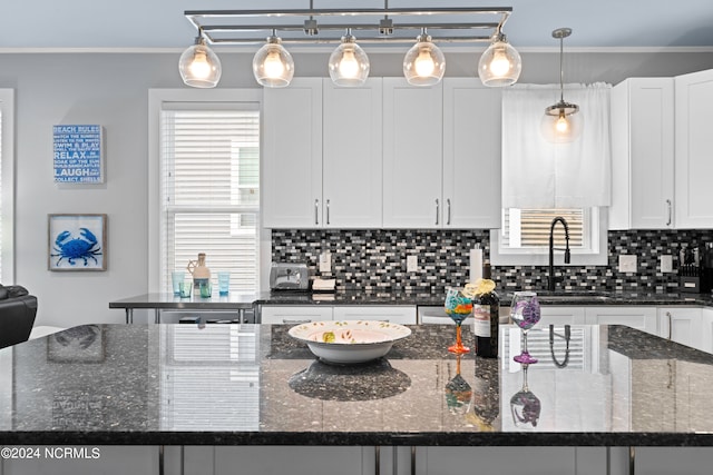 kitchen with dark stone countertops, crown molding, and pendant lighting