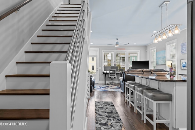 stairway featuring crown molding, dark hardwood / wood-style floors, and ceiling fan with notable chandelier