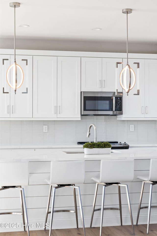 kitchen featuring white cabinetry, decorative light fixtures, light hardwood / wood-style flooring, and backsplash