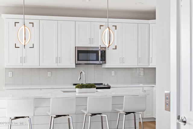 kitchen with a kitchen bar, white cabinetry, light stone counters, tasteful backsplash, and pendant lighting