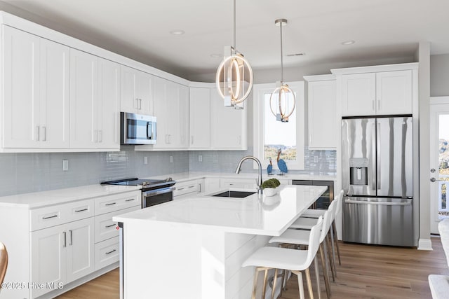 kitchen with sink, hanging light fixtures, appliances with stainless steel finishes, an island with sink, and white cabinets