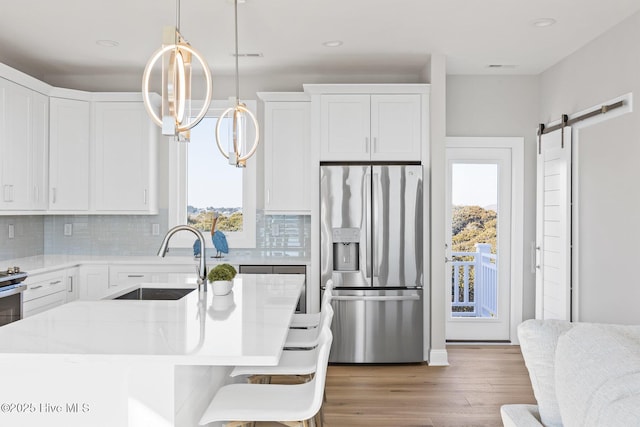 kitchen with white cabinetry, sink, hanging light fixtures, stainless steel fridge with ice dispenser, and a barn door