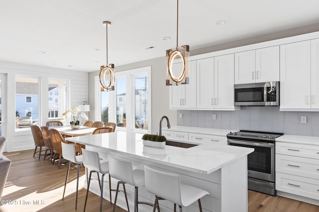 kitchen featuring appliances with stainless steel finishes, pendant lighting, sink, white cabinets, and a center island with sink