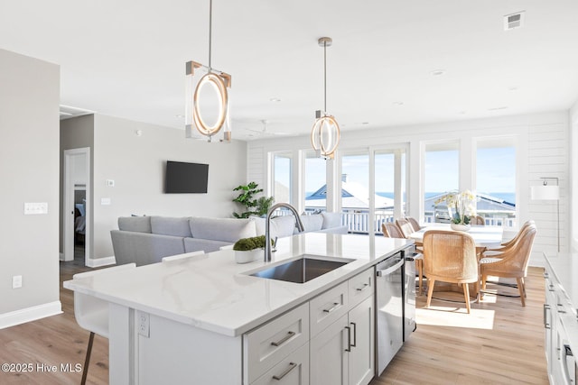 kitchen featuring sink, white cabinetry, light stone counters, an island with sink, and decorative light fixtures