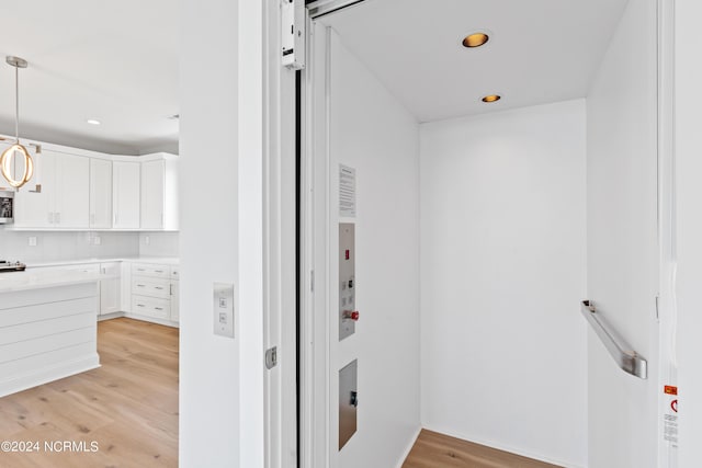 kitchen with pendant lighting, elevator, white cabinets, and light wood-type flooring