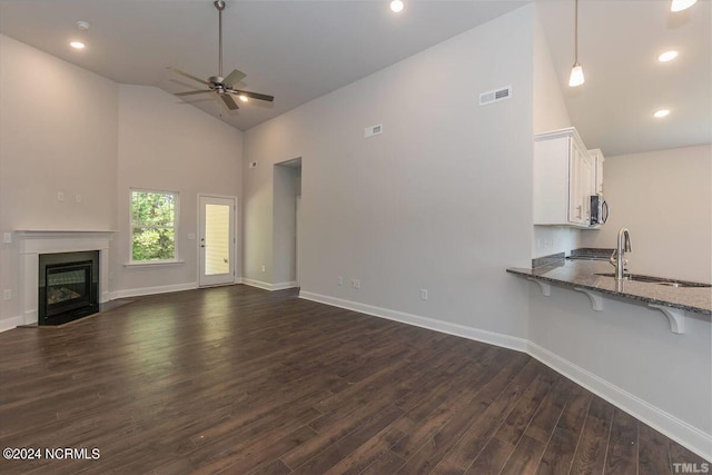 unfurnished living room featuring a sink, high vaulted ceiling, ceiling fan, dark wood-style flooring, and a fireplace with flush hearth