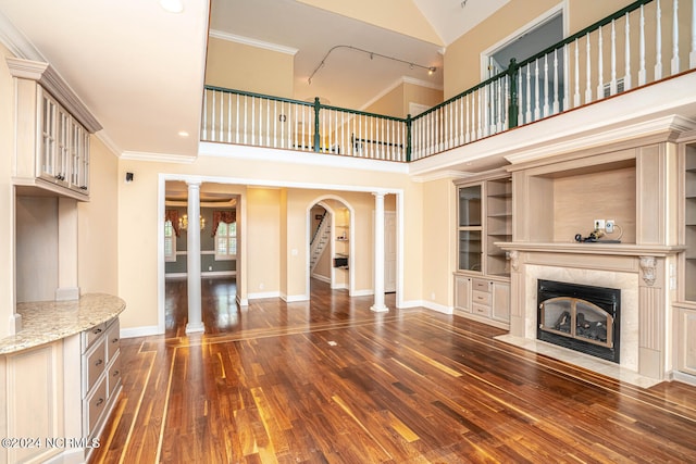 unfurnished living room featuring dark wood-type flooring, a towering ceiling, decorative columns, and a high end fireplace