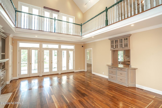 unfurnished living room featuring french doors, ornamental molding, a towering ceiling, and dark hardwood / wood-style flooring