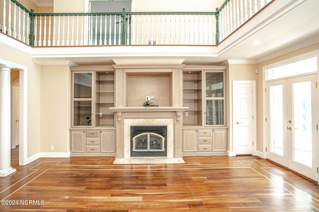 unfurnished living room with french doors, a high ceiling, a fireplace, crown molding, and hardwood / wood-style floors