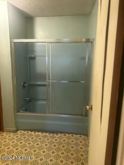 bathroom featuring a textured ceiling, bath / shower combo with glass door, and tile flooring