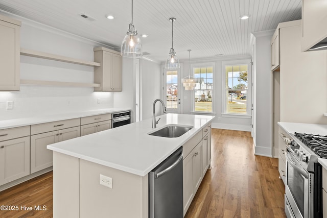 kitchen featuring appliances with stainless steel finishes, sink, decorative light fixtures, dark hardwood / wood-style floors, and a center island with sink