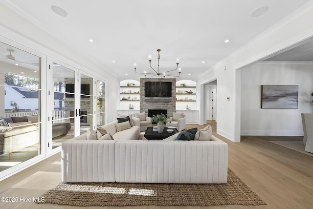 living room with light wood finished floors, a large fireplace, crown molding, and an inviting chandelier