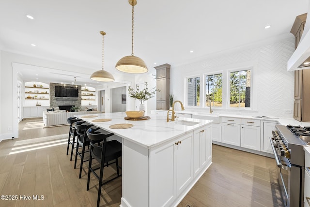 kitchen featuring light wood finished floors, light stone countertops, a center island with sink, a fireplace, and a sink