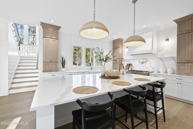 kitchen with an island with sink, ornamental molding, light wood-style floors, a kitchen bar, and backsplash