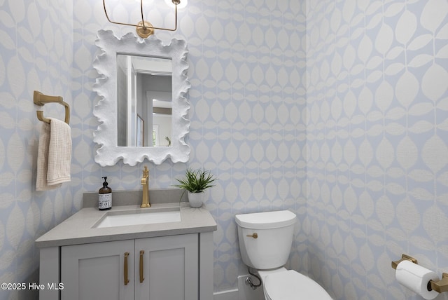 half bathroom featuring wallpapered walls, toilet, and vanity