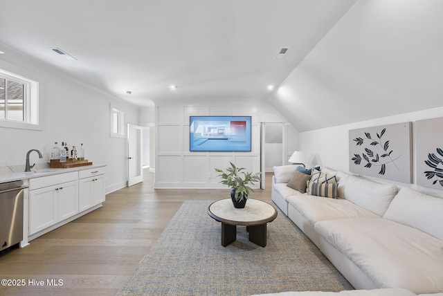 living room with indoor wet bar, vaulted ceiling, light wood-style floors, and visible vents