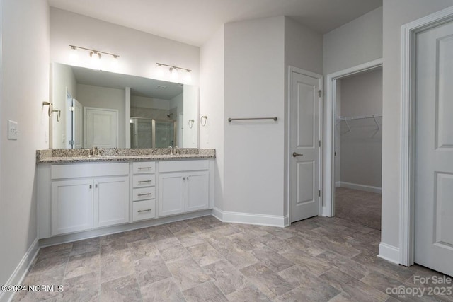 full bath with a sink, double vanity, a stall shower, baseboards, and a spacious closet
