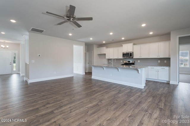 kitchen featuring dark hardwood / wood-style flooring, light stone countertops, an island with sink, appliances with stainless steel finishes, and white cabinetry