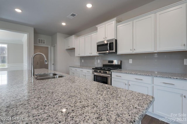 kitchen with light stone counters, white cabinets, stainless steel appliances, and sink