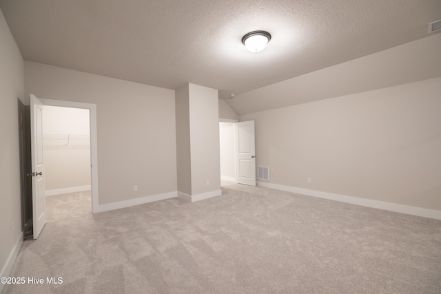 unfurnished bedroom with a closet, a textured ceiling, vaulted ceiling, light carpet, and a walk in closet