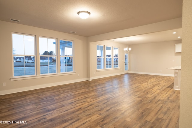 unfurnished living room with hardwood / wood-style flooring, a water view, an inviting chandelier, and a textured ceiling