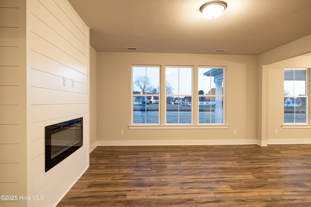 unfurnished living room with a fireplace, a textured ceiling, and dark hardwood / wood-style floors