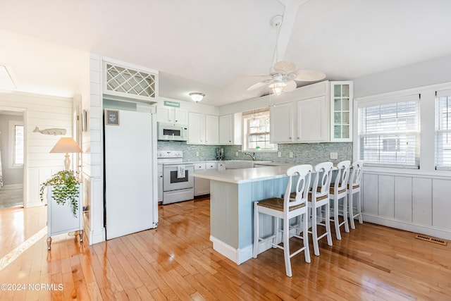 kitchen with light hardwood / wood-style floors, kitchen peninsula, white appliances, and a wealth of natural light