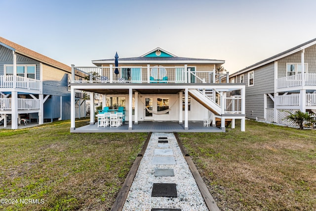 back house at dusk with a wooden deck, a yard, and a patio area