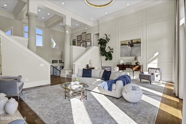 living room with crown molding, dark wood-type flooring, a high ceiling, and ornate columns