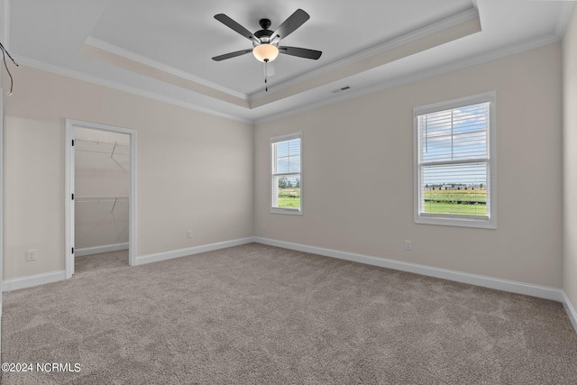 empty room featuring ceiling fan, light colored carpet, a tray ceiling, and ornamental molding